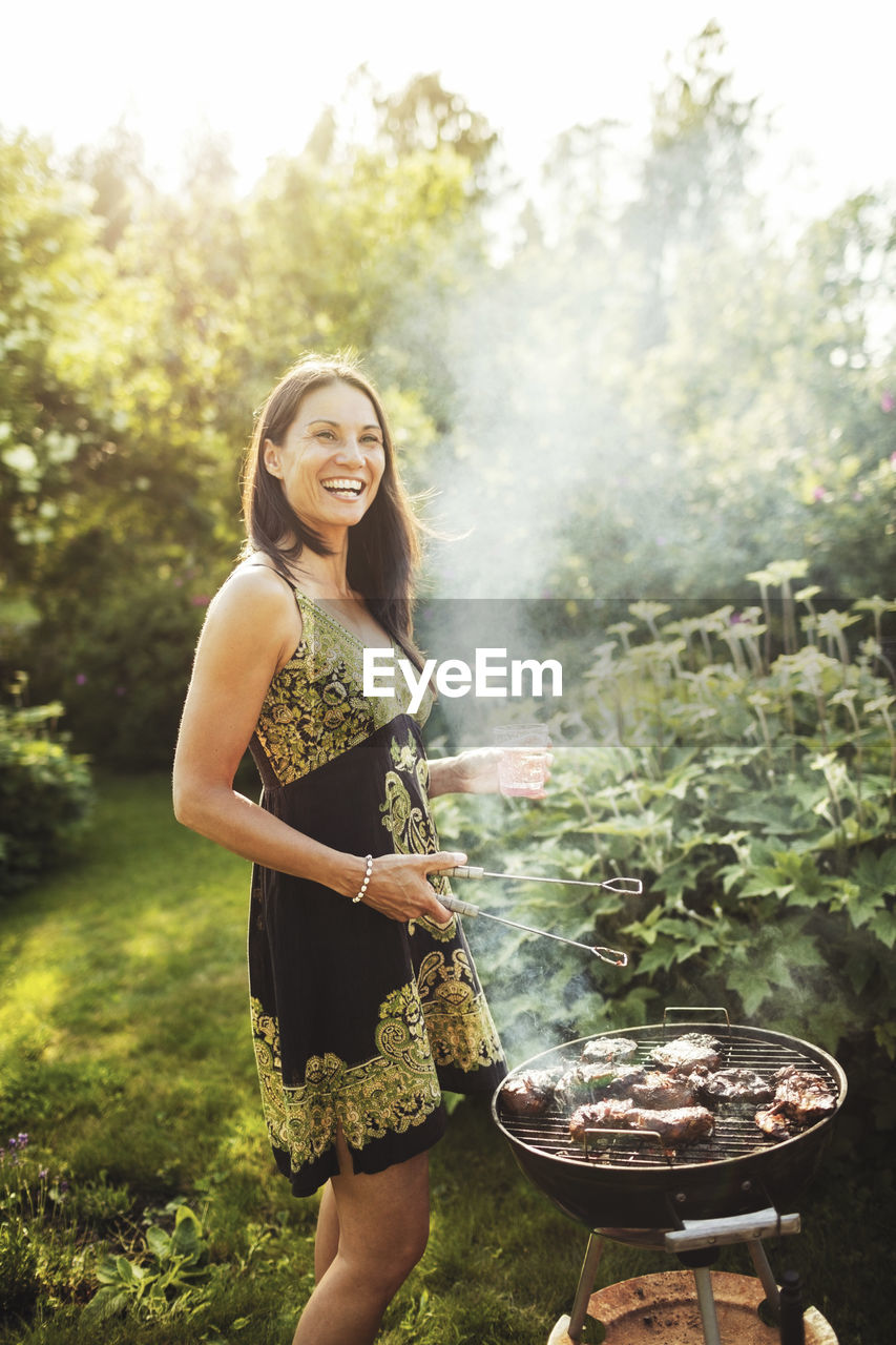Happy woman standing by barbecue in back yard