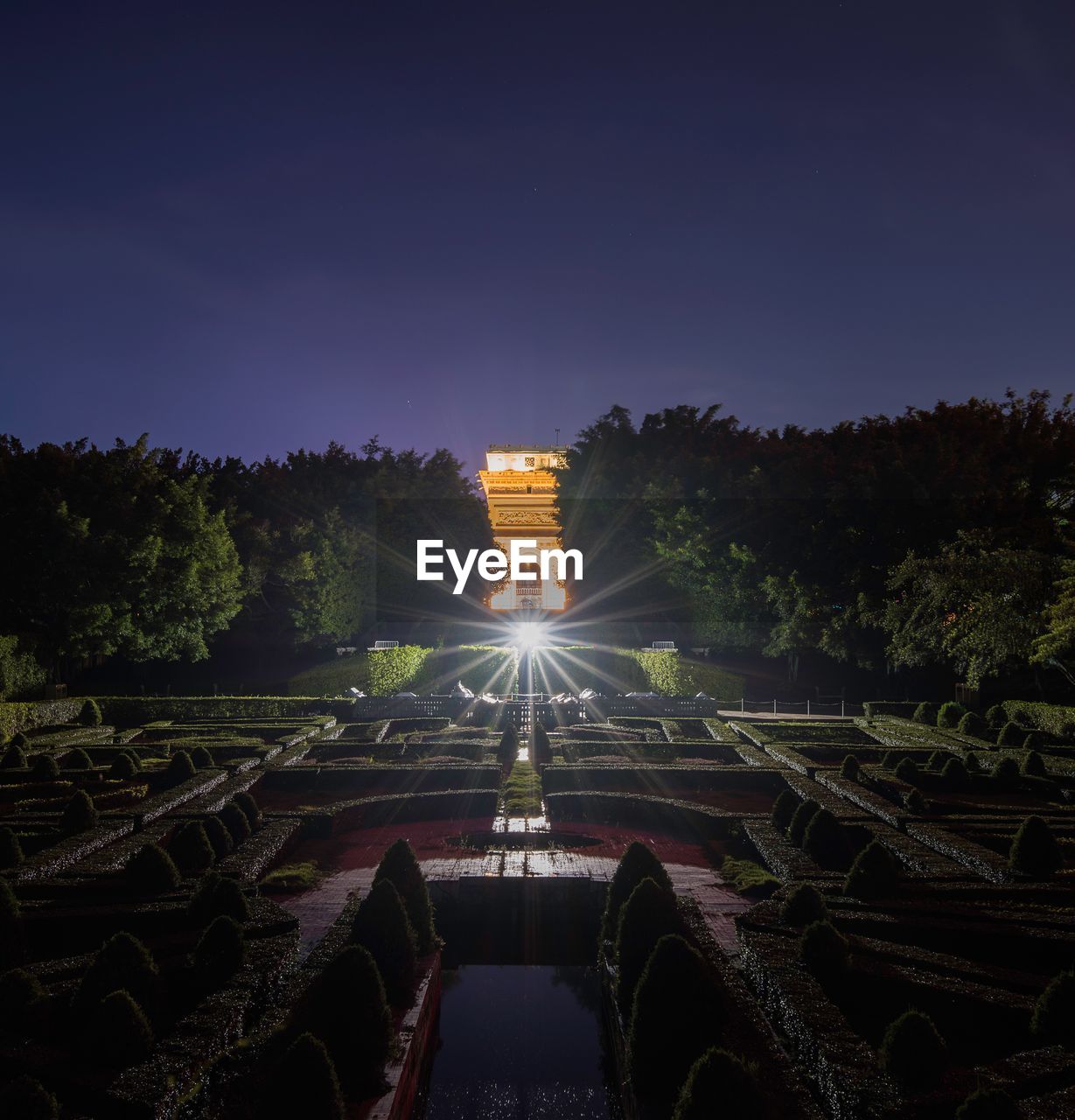 ILLUMINATED BUILT STRUCTURE AGAINST TREES AT NIGHT