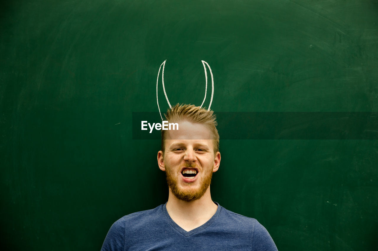 Portrait of young man with horned tattoo on blackboard