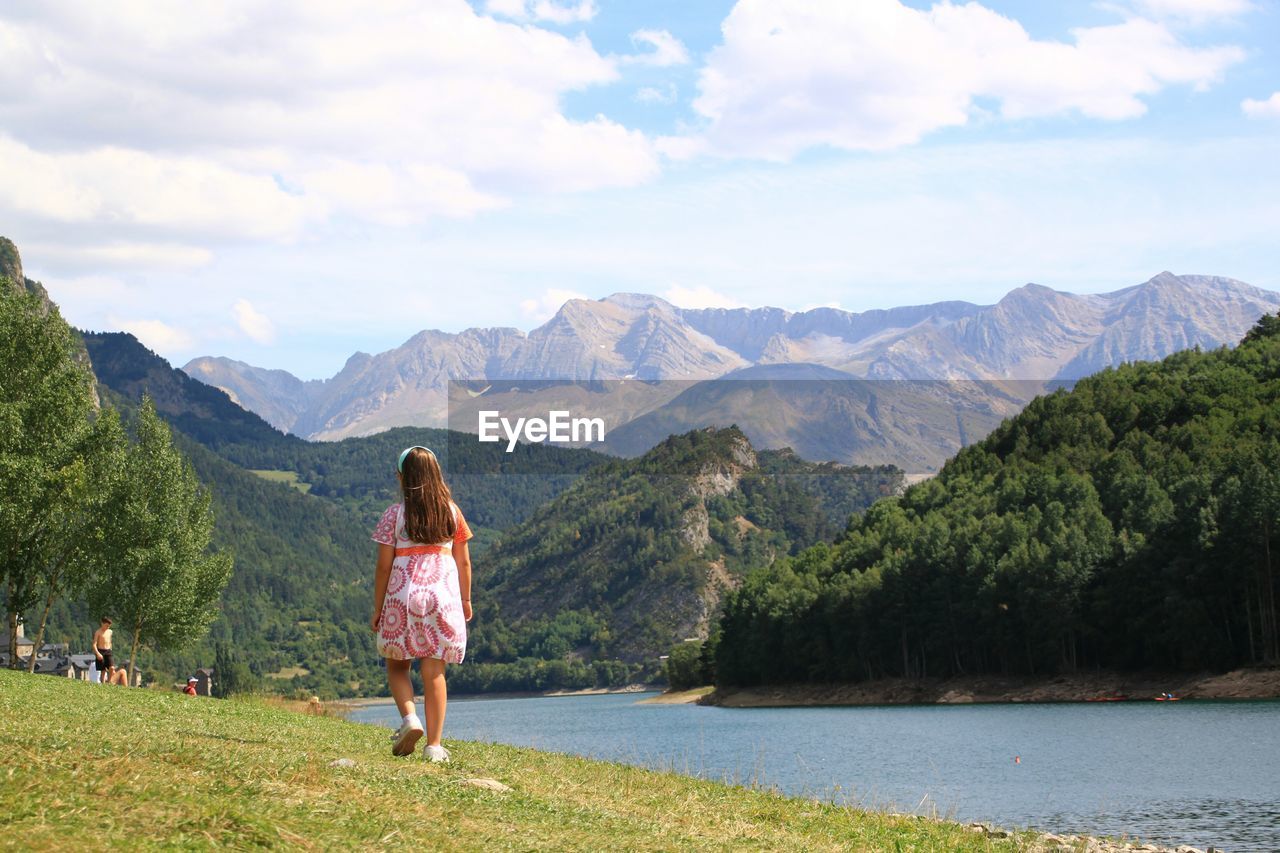 Rear view of young girl walking by lake against mountains