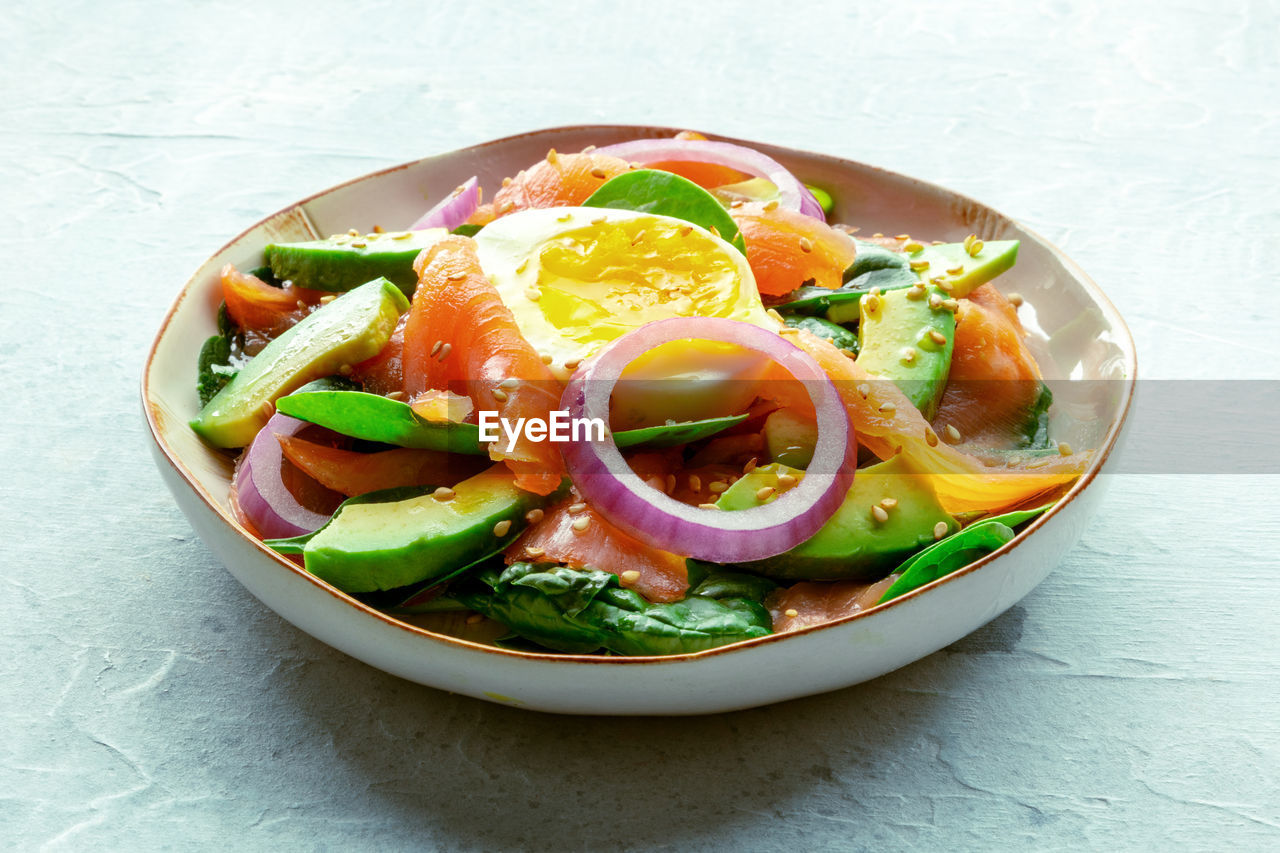Salmon, avocado and egg salad with fresh leaves and onions, on a slate background. healthy diet