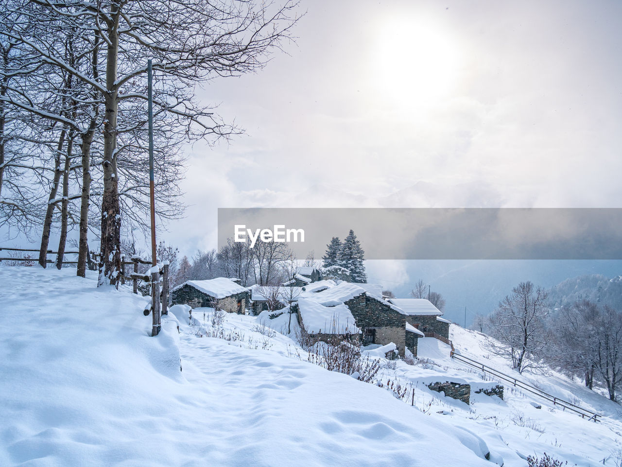 winter, snow, cold temperature, tree, environment, landscape, scenics - nature, nature, forest, beauty in nature, land, sky, plant, mountain, tranquil scene, mountain range, architecture, tranquility, fog, sun, rural scene, woodland, white, frozen, freezing, travel, travel destinations, building, cloud, non-urban scene, house, coniferous tree, no people, built structure, pine tree, pinaceae, sunlight, blue, holiday, tourism, outdoors, pine woodland, morning, idyllic, building exterior, piste, ice, footwear, hut, vacation, landscaped, polar climate, trip, frost, snowing, snowcapped mountain, lens flare