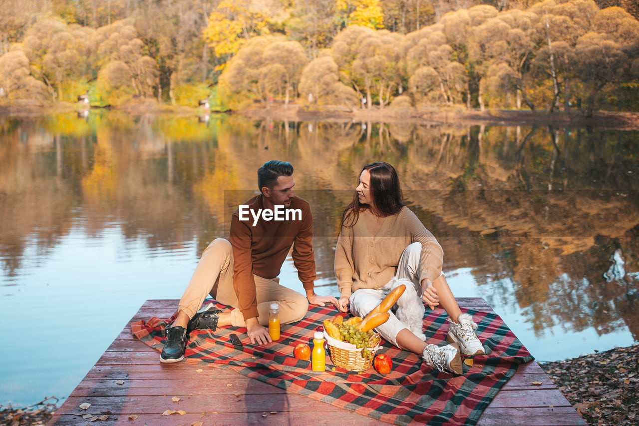 Cheerful couple sitting with dog on pier by lake