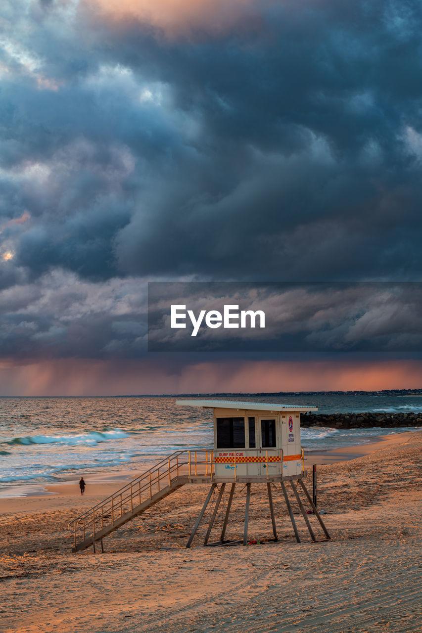 Scenic view of beach and life saver hut against stormy sky during sunset