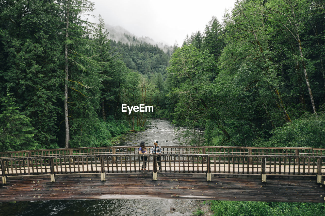 A young couple enjoys a hike on a bridge in the pacific northwest.