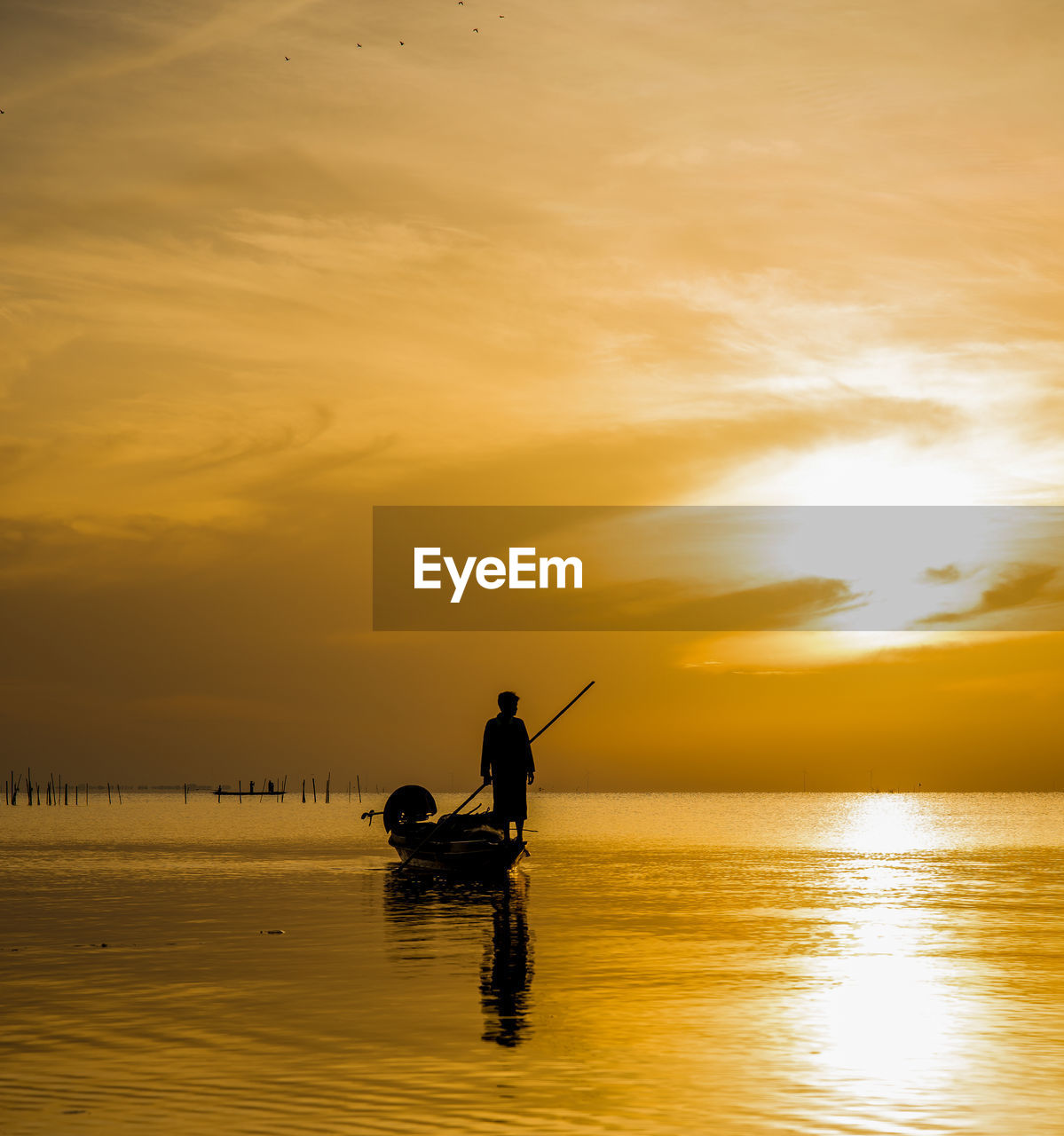 Silhouette man standing on fishing boat against sky during sunset