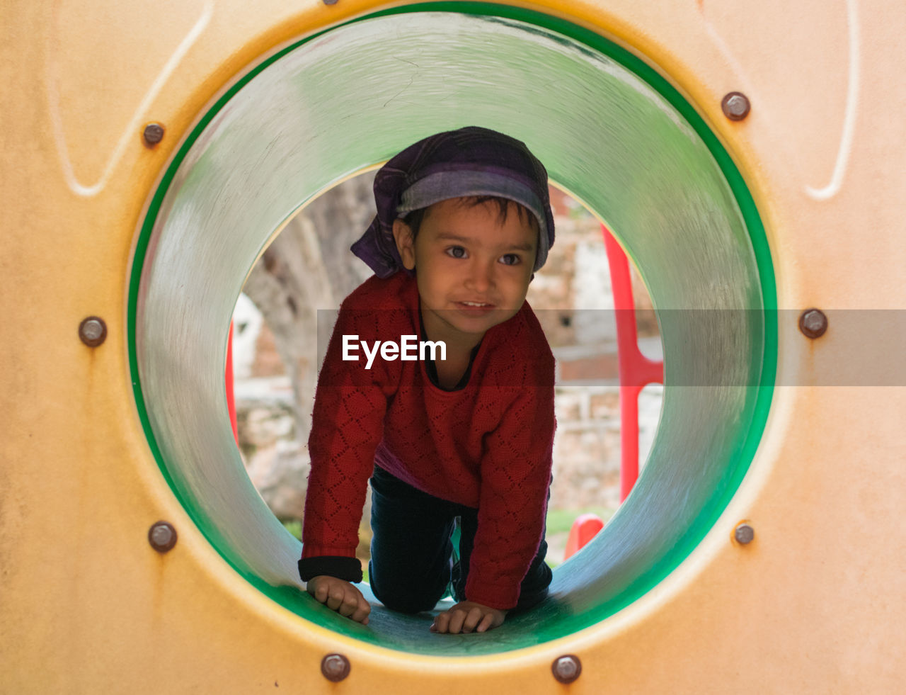 Full length of cute girl kneeling in outdoor play equipment in playground