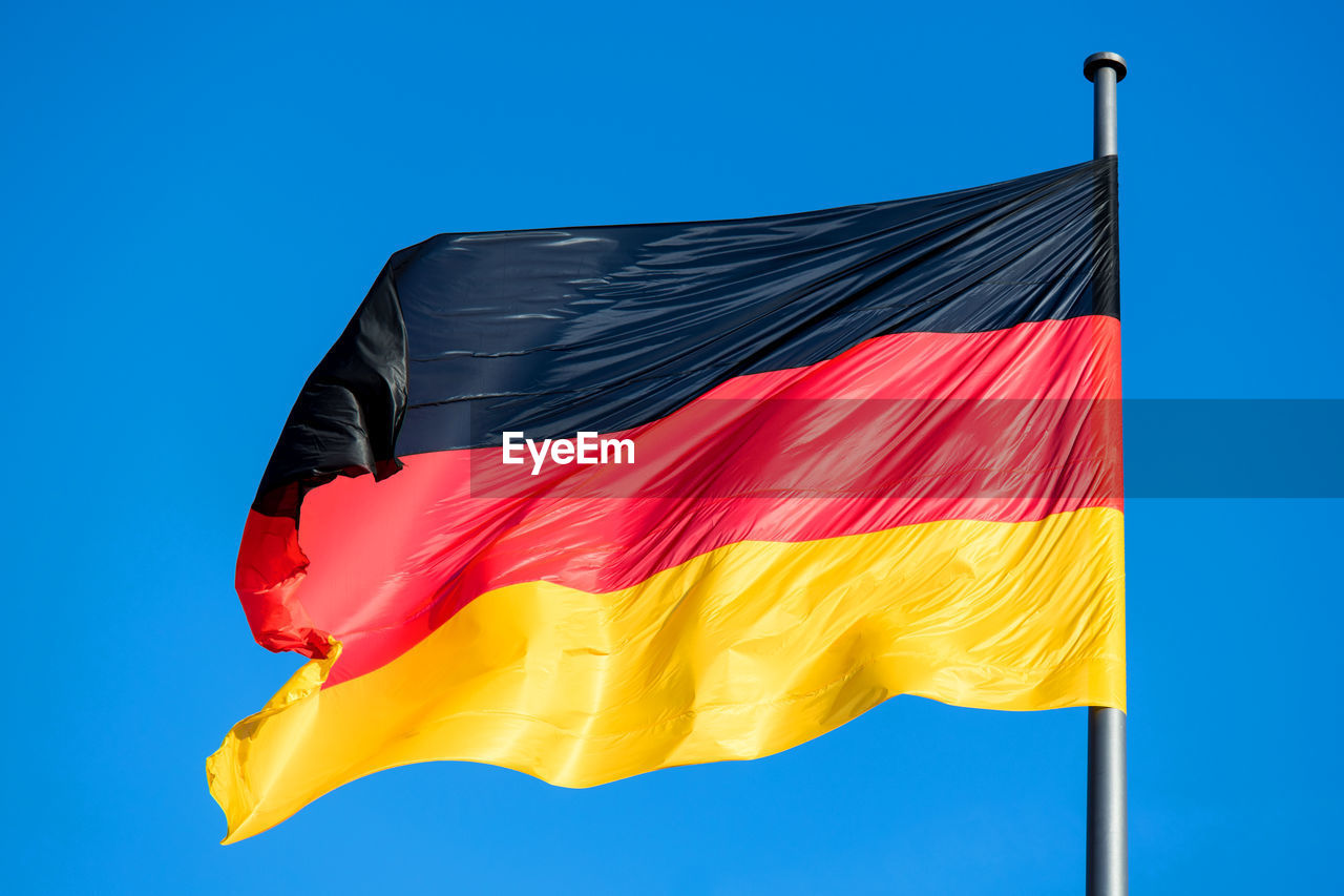 flag, blue, patriotism, wind, red, environment, yellow, no people, sky, nature, striped, pride, red flag, multi colored, clear sky, symbol, low angle view, outdoors, pole, textile, day, copy space, orange