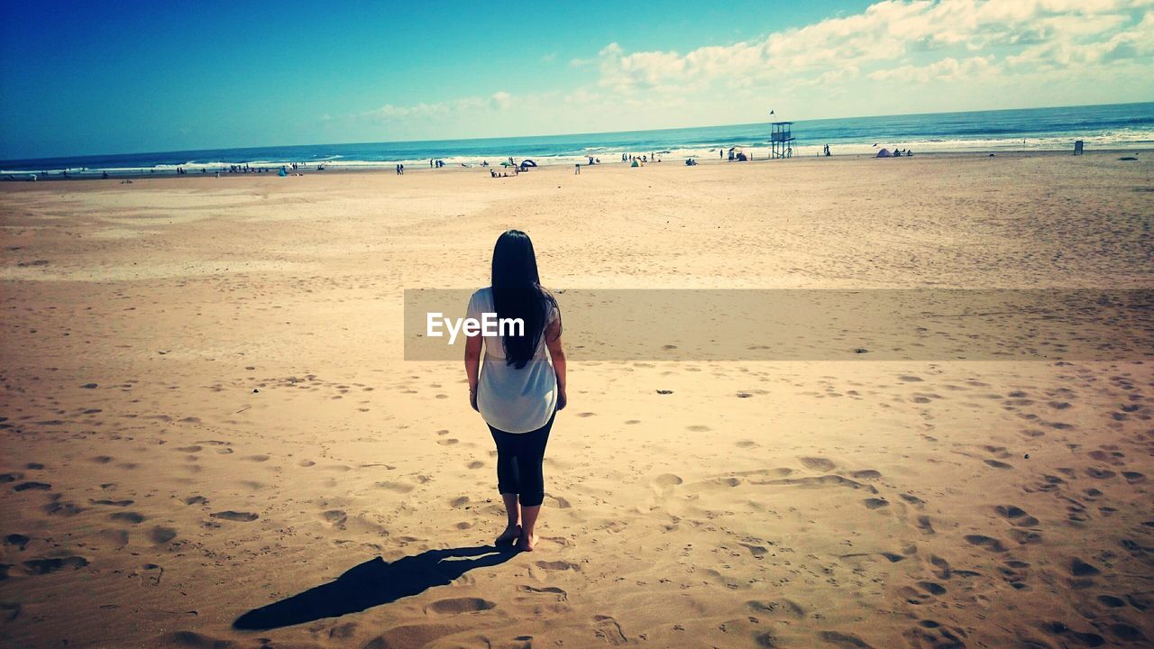 REAR VIEW OF WOMAN STANDING AT BEACH