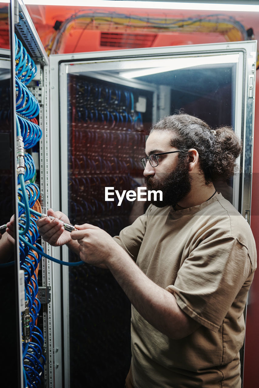 It technician with beard connecting cables in server room