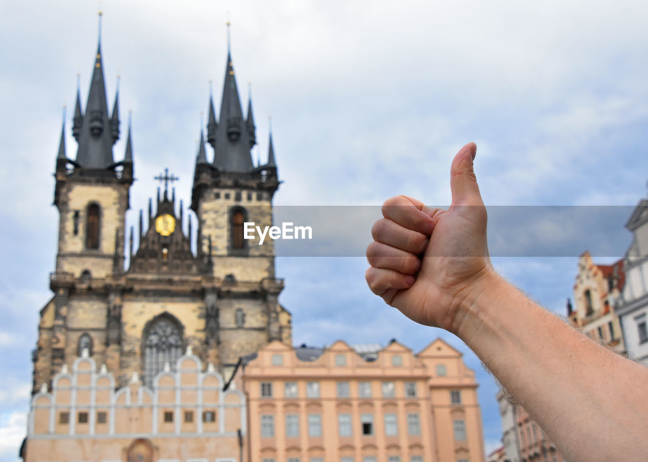Cropped image of hand gesturing against cathedral in city