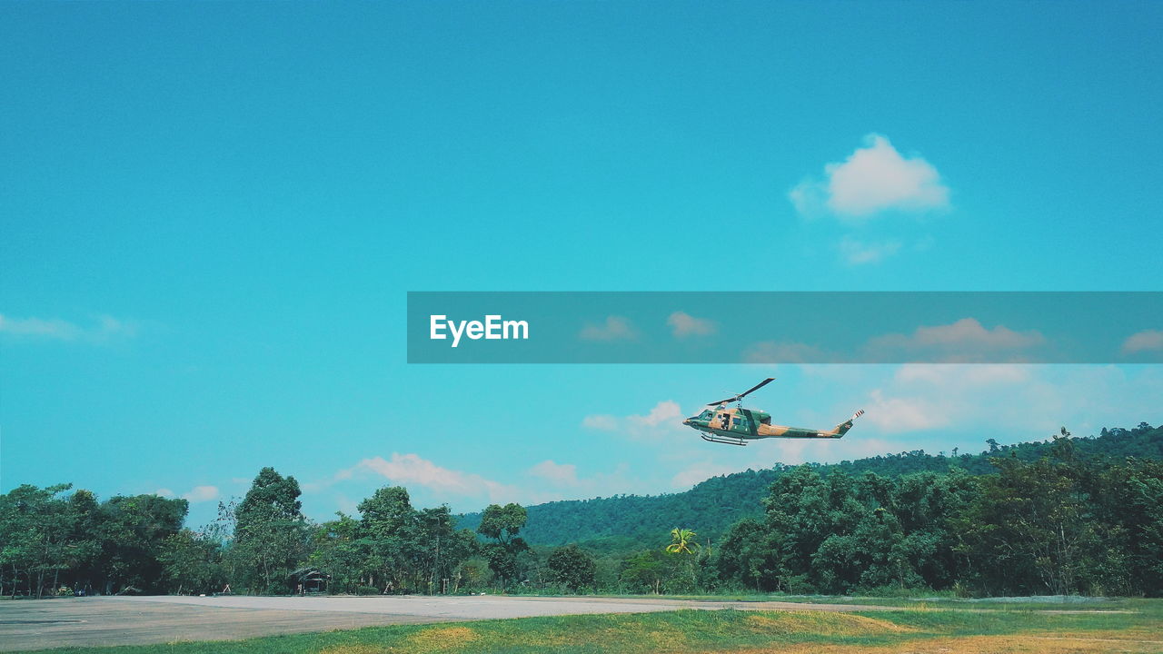 AIRPLANE FLYING OVER TREES AGAINST SKY