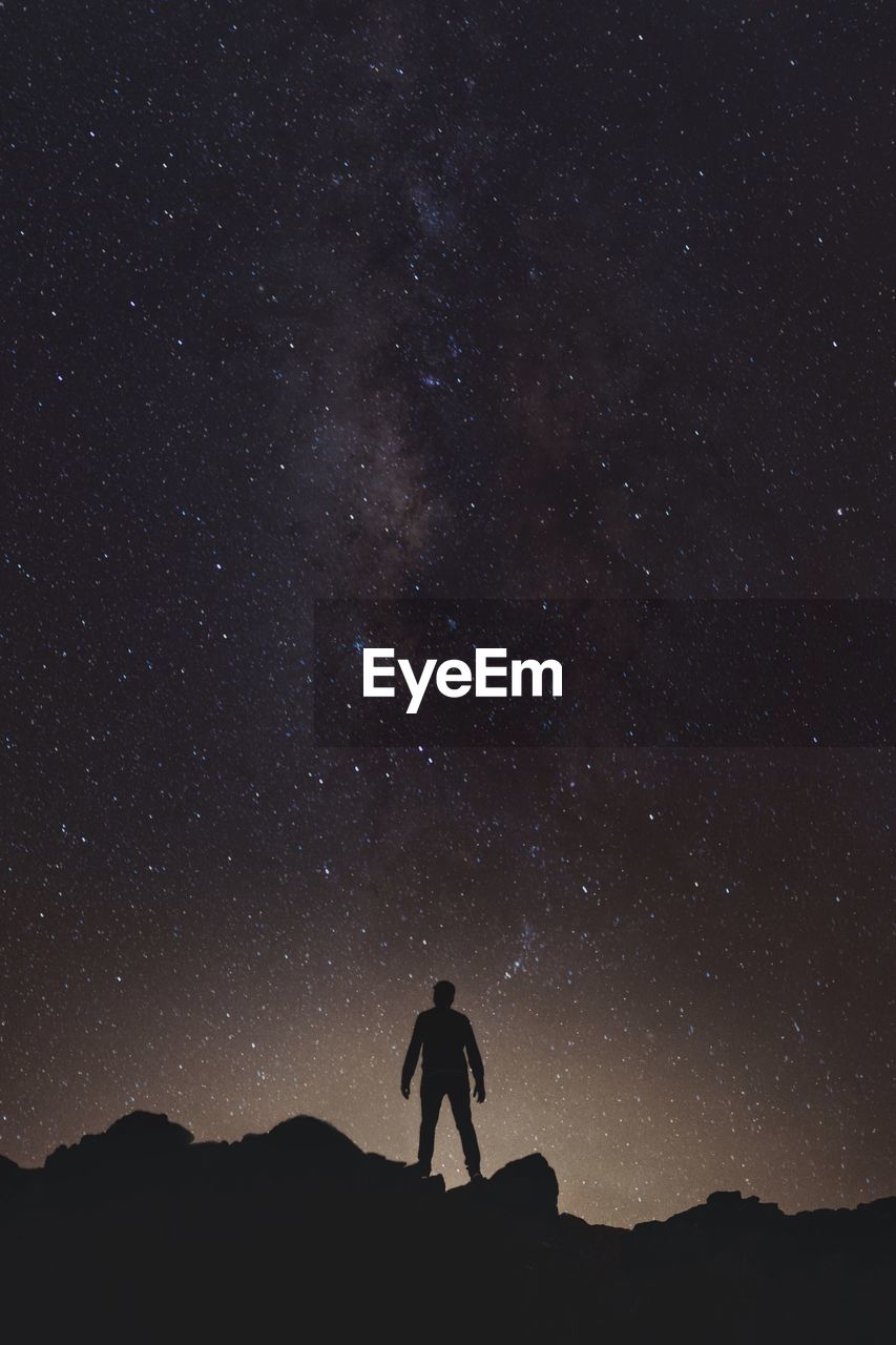 Silhouette man standing on rock formation against milky way