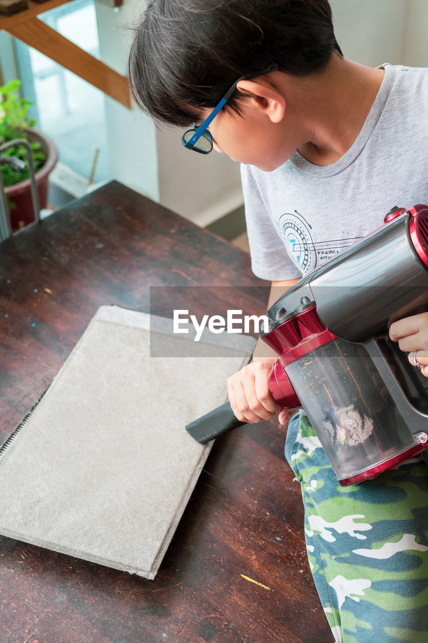 Cute boy using vacuum cleaner at home