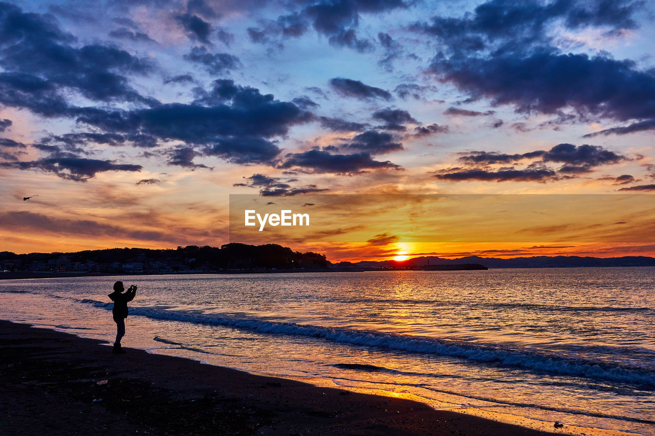 Silhouette person standing on beach against sky during sunrise