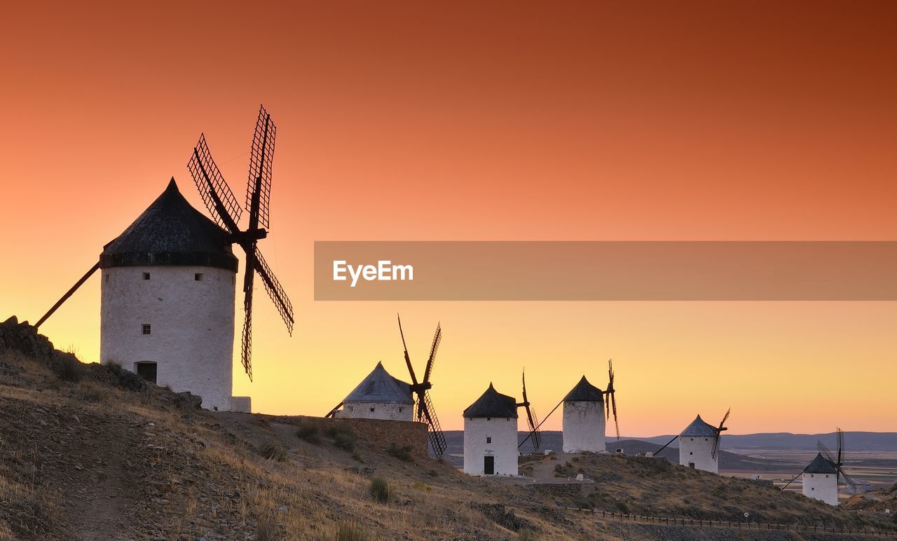 TRADITIONAL WINDMILL ON LAND BY BUILDING AGAINST SKY DURING SUNSET