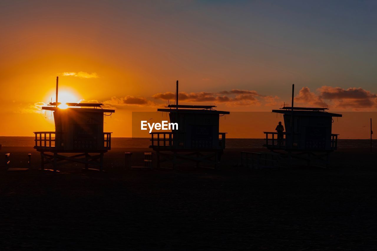 Silhouette built structure on beach against sky during sunset