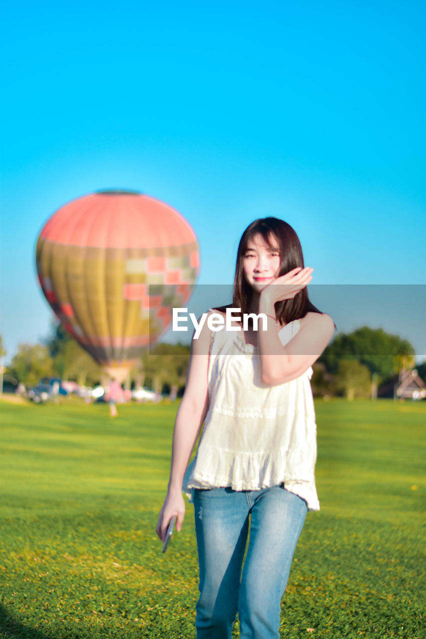 Young woman with balloons on field against clear blue sky