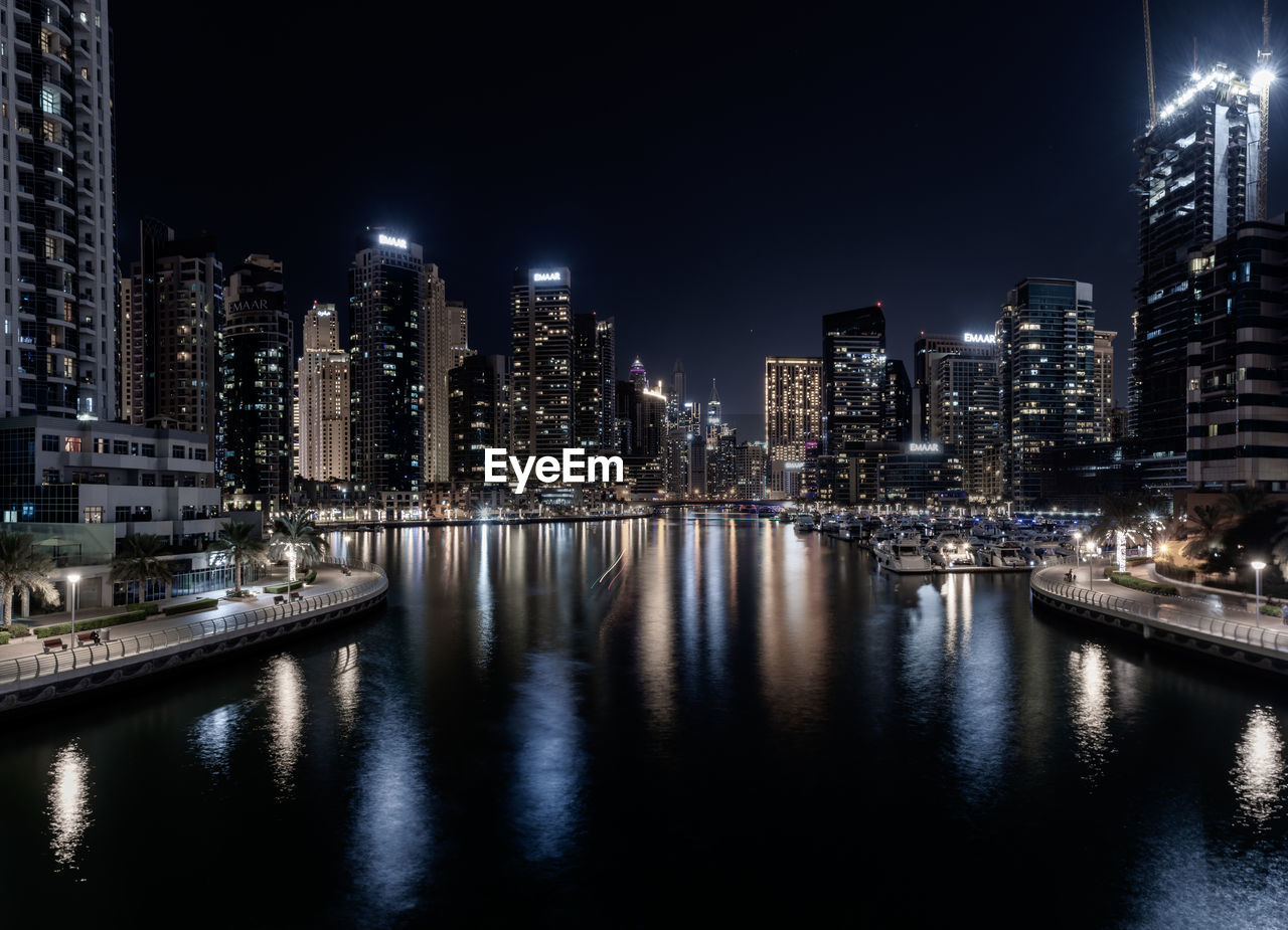 ILLUMINATED BUILDINGS BY RIVER AGAINST SKY AT NIGHT IN CITY