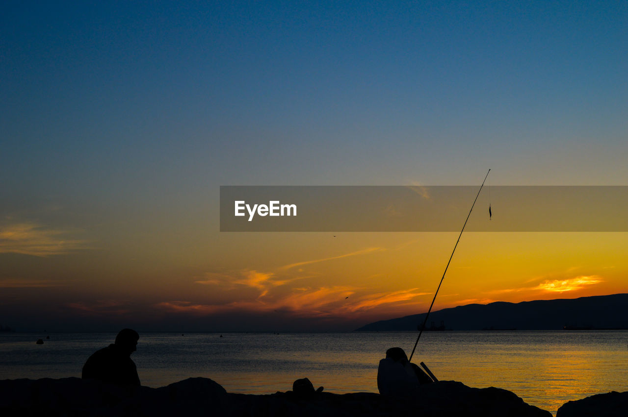 Silhouette people fishing at sea against sky during sunset