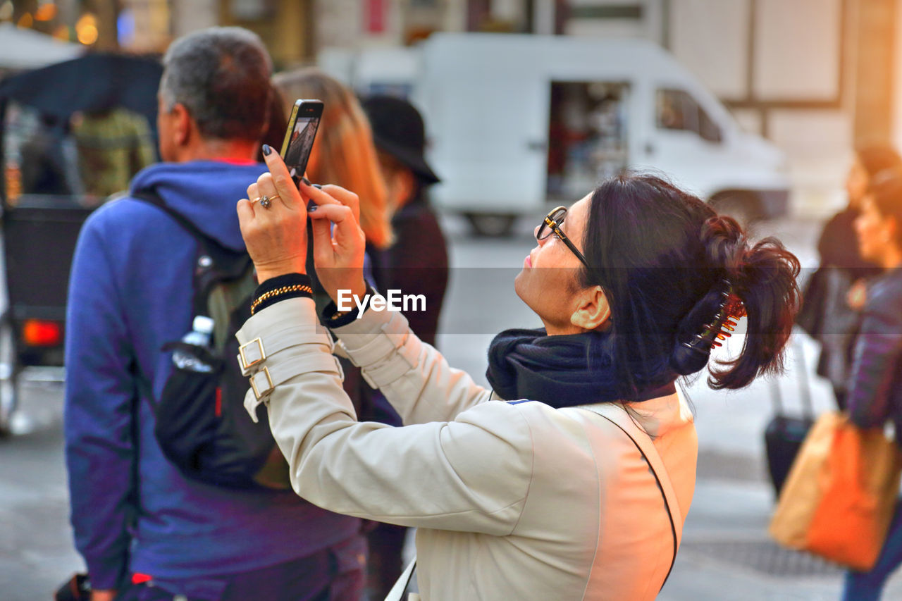 REAR VIEW OF MAN AND WOMAN USING SMART PHONE WHILE STANDING ON LAPTOP