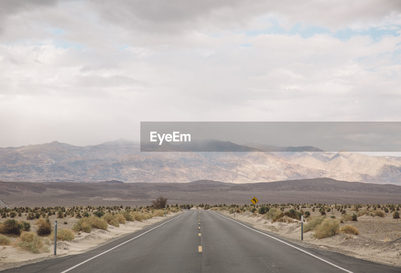 Road by mountains against sky