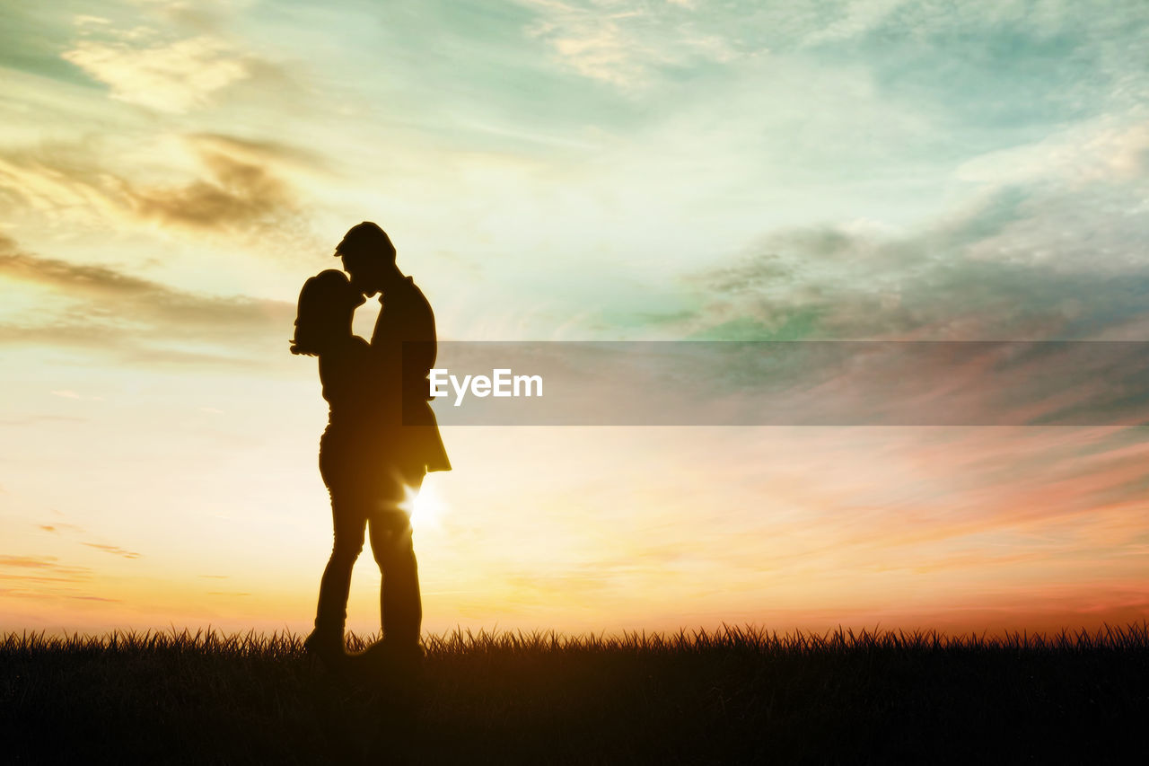 SILHOUETTE COUPLE STANDING ON FIELD AGAINST SKY DURING SUNSET