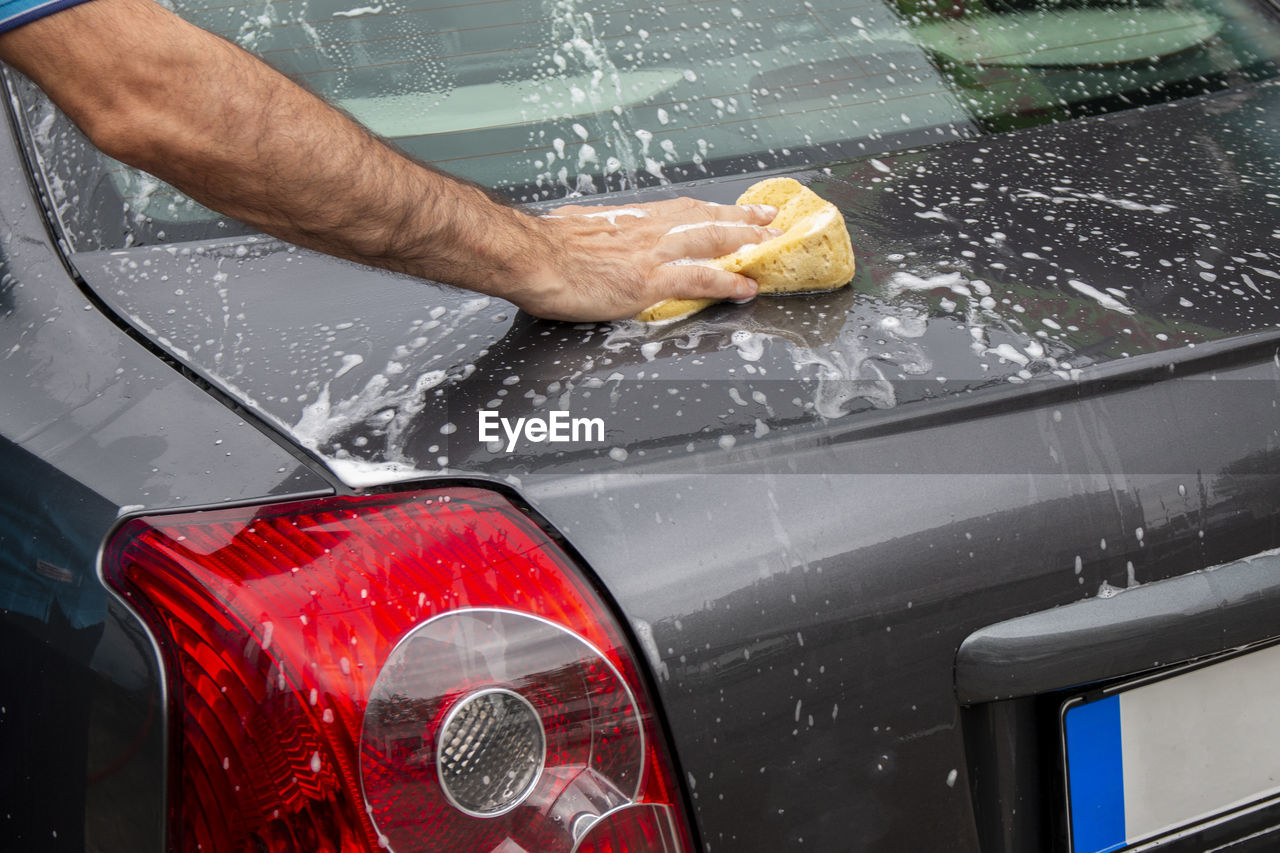 Man cleans automobile with covered with foam shampoo chemical detergents during carwash self service