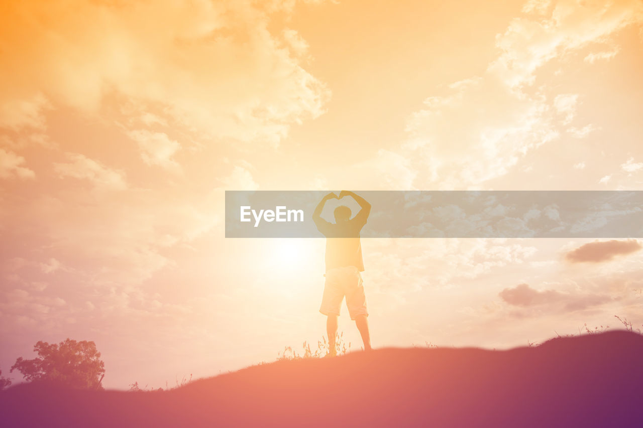 Rear view of man standing on mountain against sky during sunset