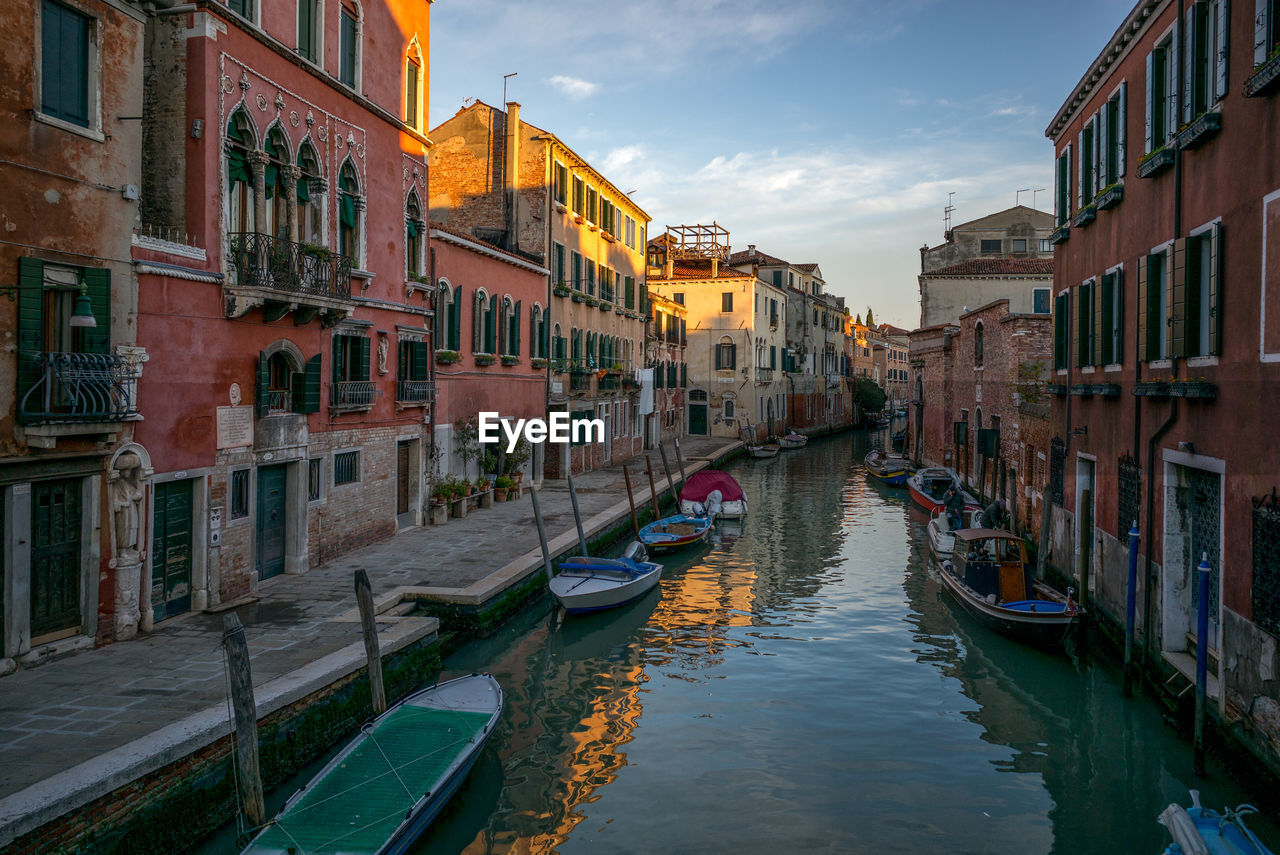 Boats moored in canal amidst buildings against sky