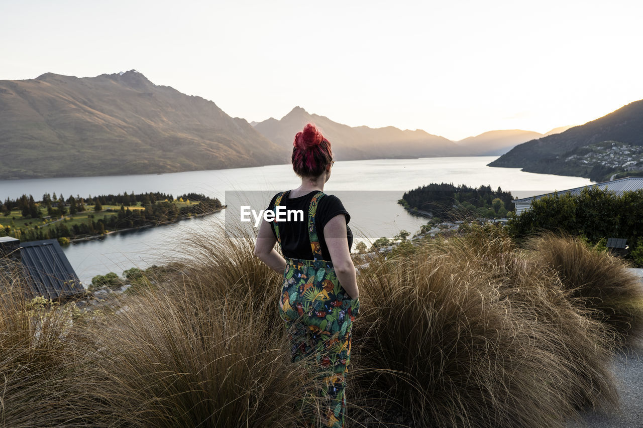 Woman overlooking queenstown and lake, at sunset in new zealand