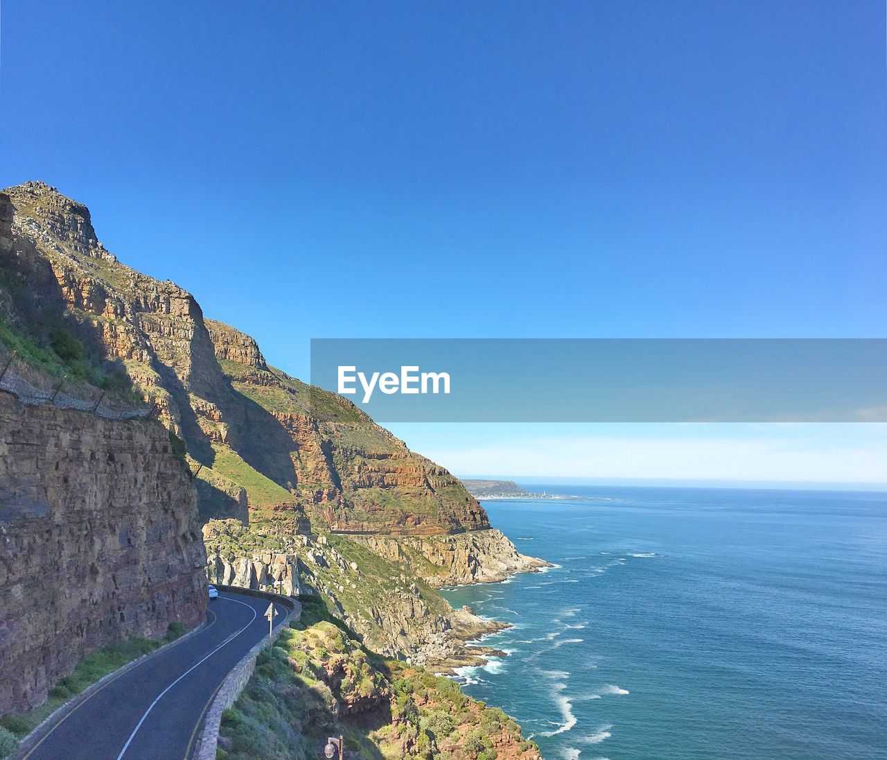 Coastal road by cliff and sea against blue sky