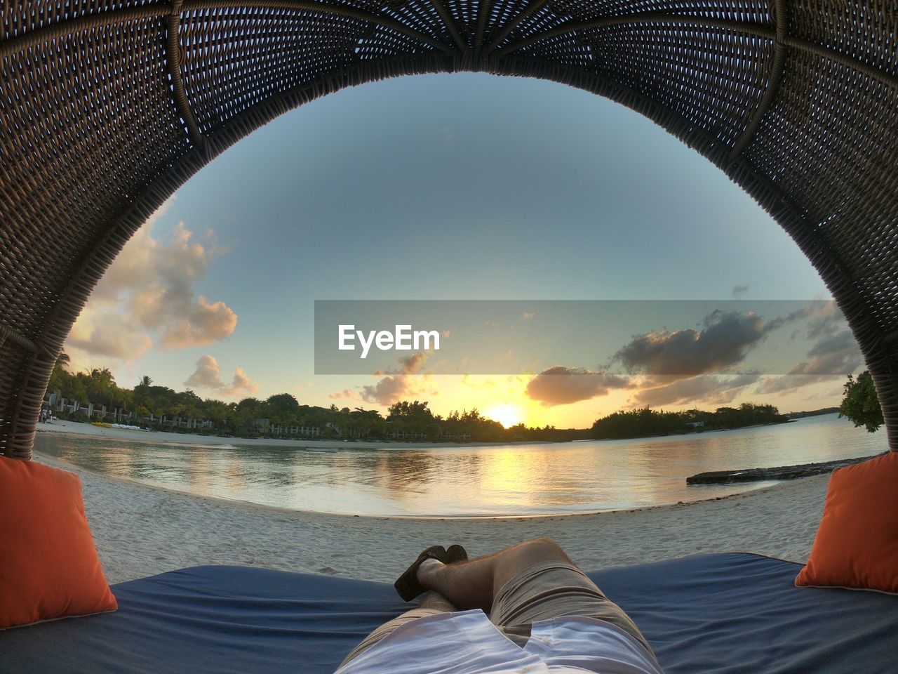 Low section of man relaxing on shore during sunset