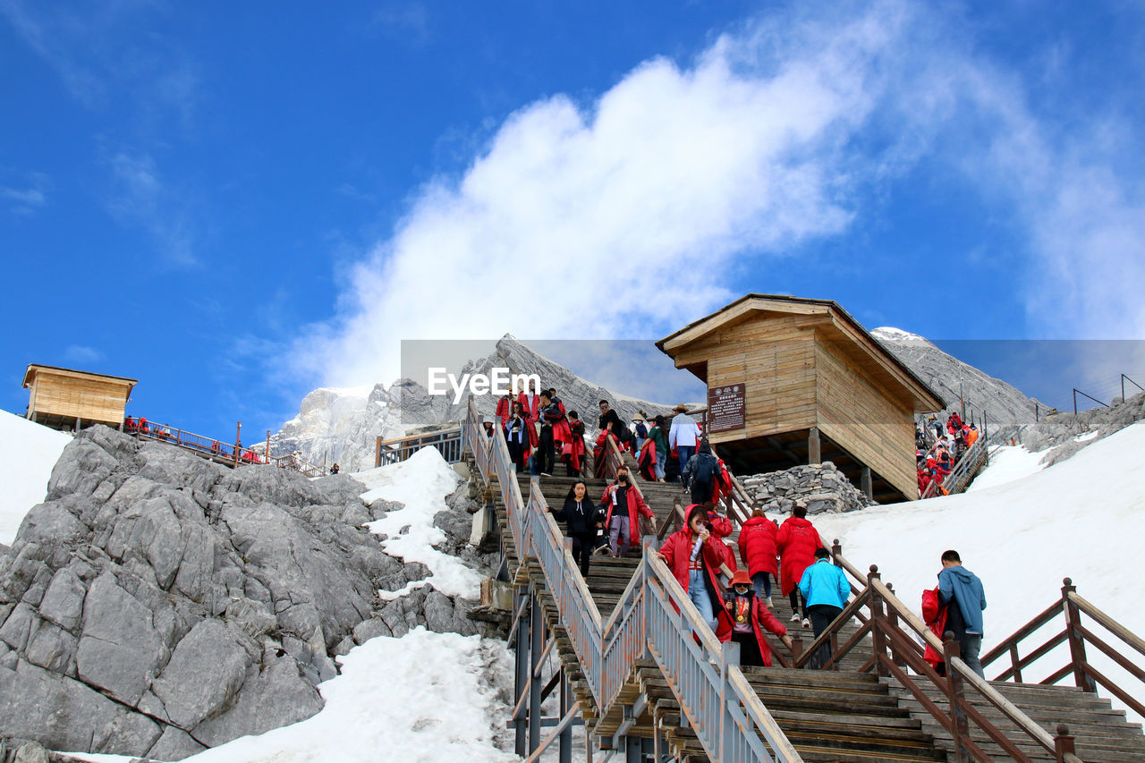 Low angle view of people on snowcapped mountain against sky