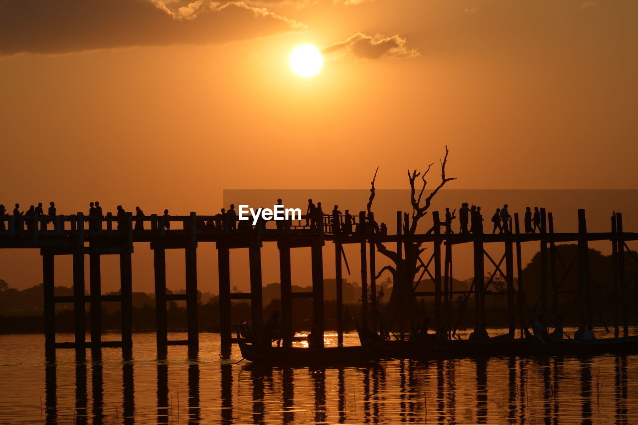 Silhouette people on footbridge over sea against sky during sunset