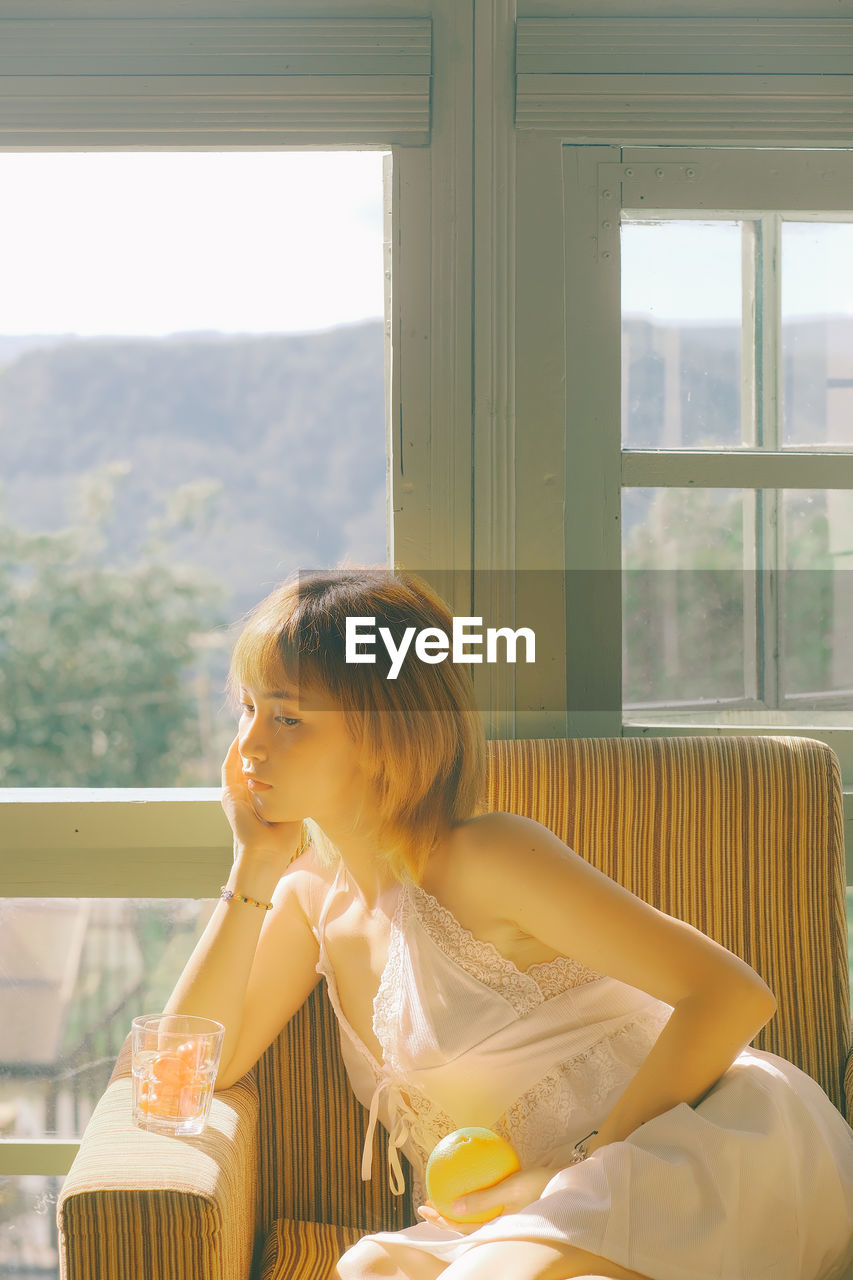 Woman looking away while sitting in chair at home