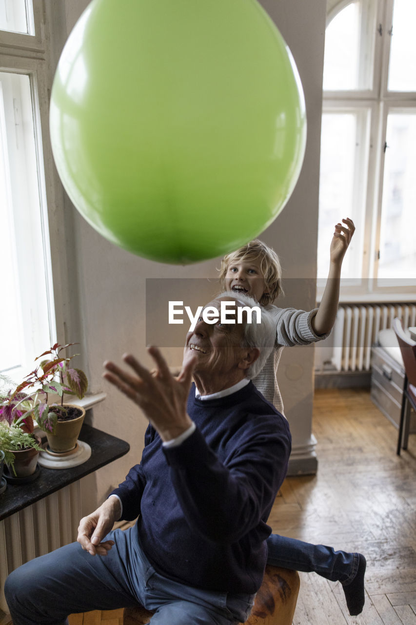 Happy grandfather and grandson playing with balloon at home