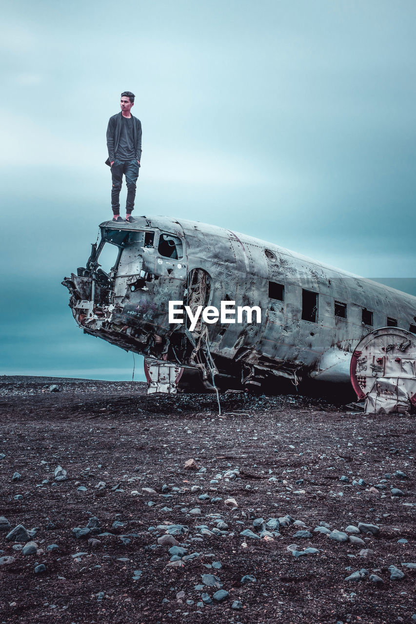 Man standing on old abandoned airplane against cloudy sky