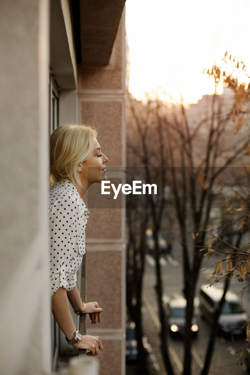 Side view of relaxed woman standing at house window