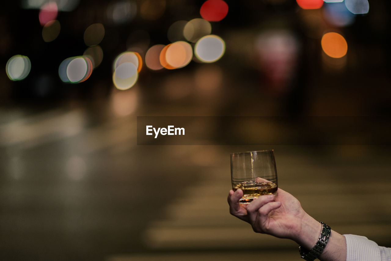 Close-up of hand holding alcohol glass on street at night