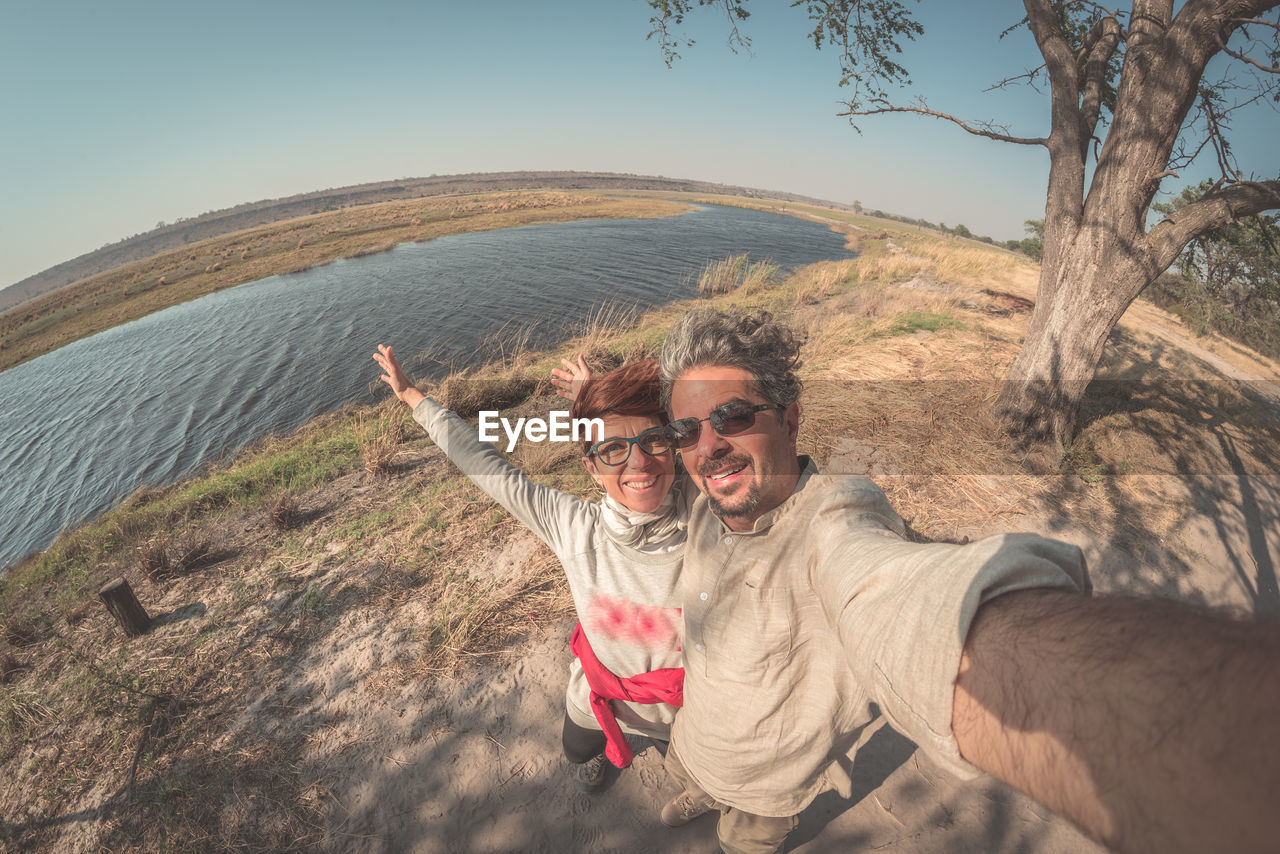 High angle view of couple standing on field by river against sky