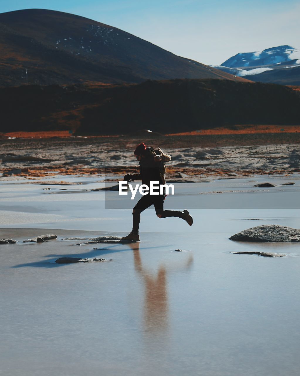 Side view of man jumping over salt lake on sunny day