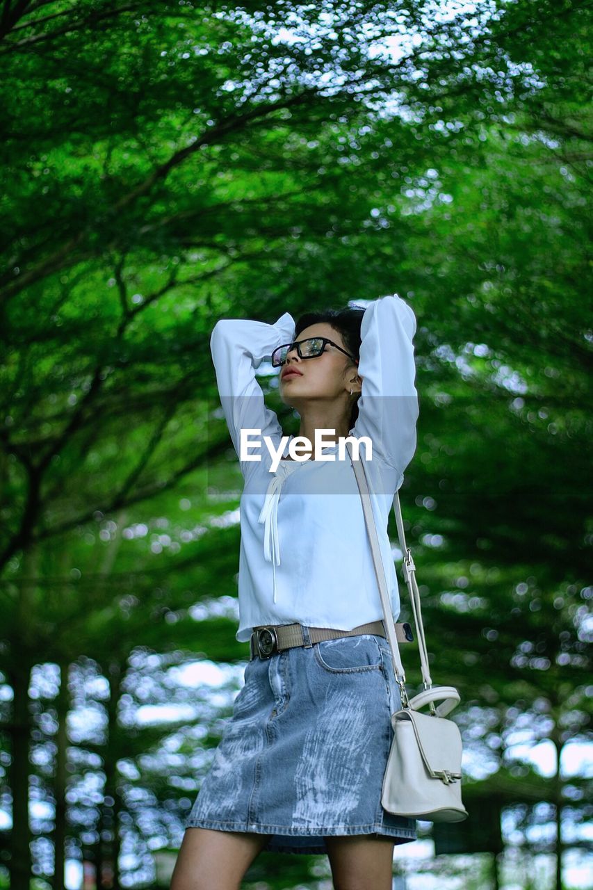 Young woman wearing sunglasses while standing against trees