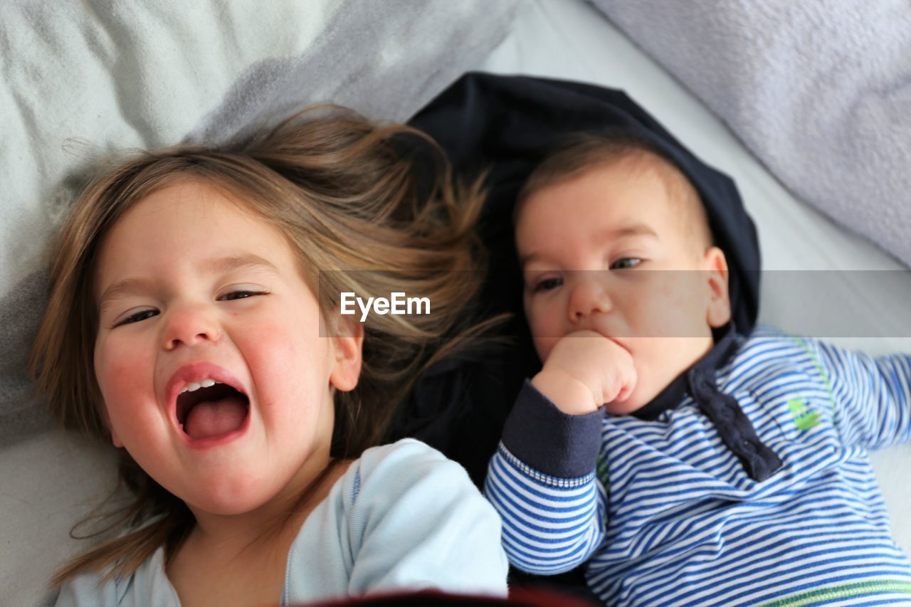 Portrait of girl lying down with brother on bed at home