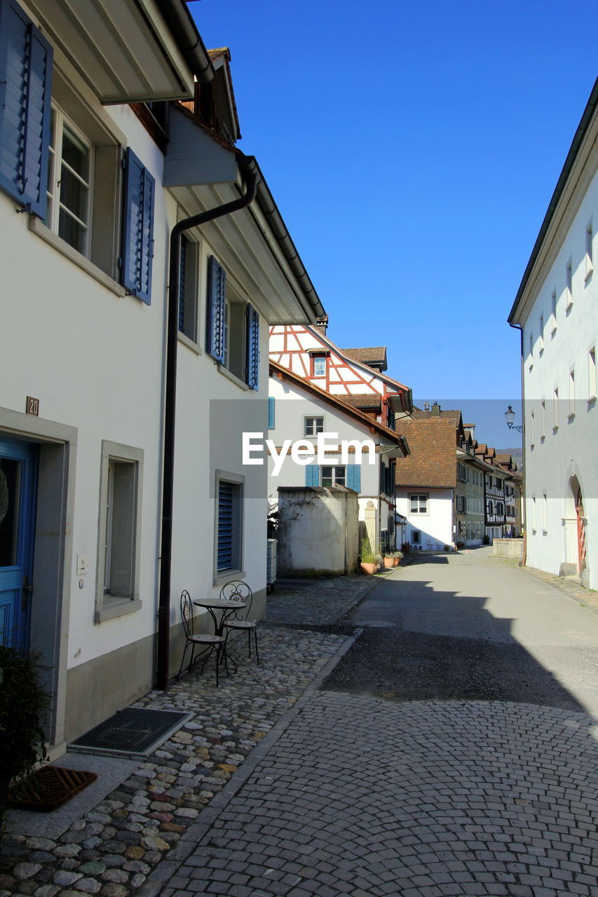 Alley amidst houses in town against clear blue sky