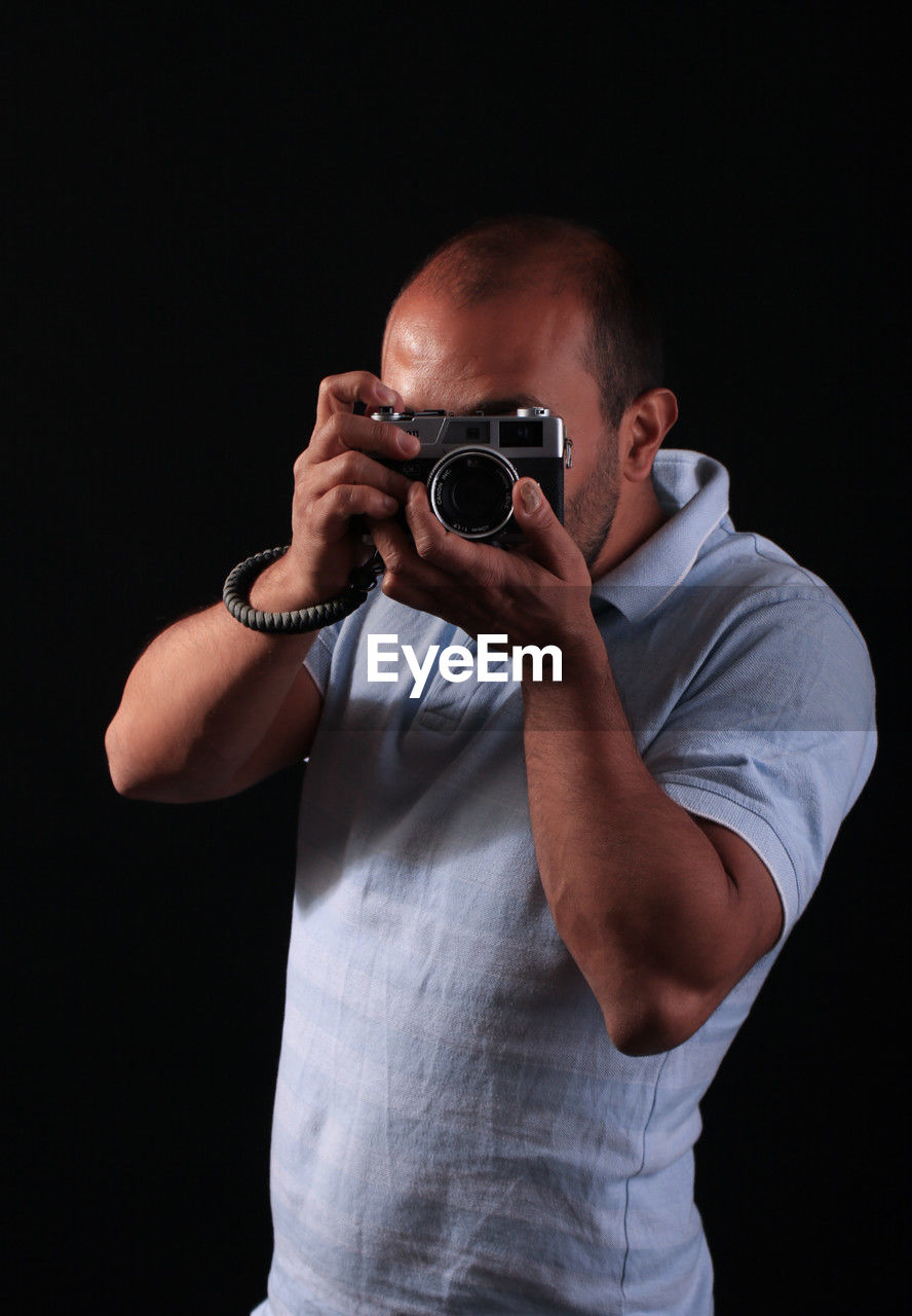 one person, black background, men, holding, studio shot, adult, waist up, portrait, camera, activity, person, occupation, technology, indoors, standing, cut out, arm, front view, professional occupation, singing, photographing, photographer, casual clothing, hand, looking at camera, copy space, clothing