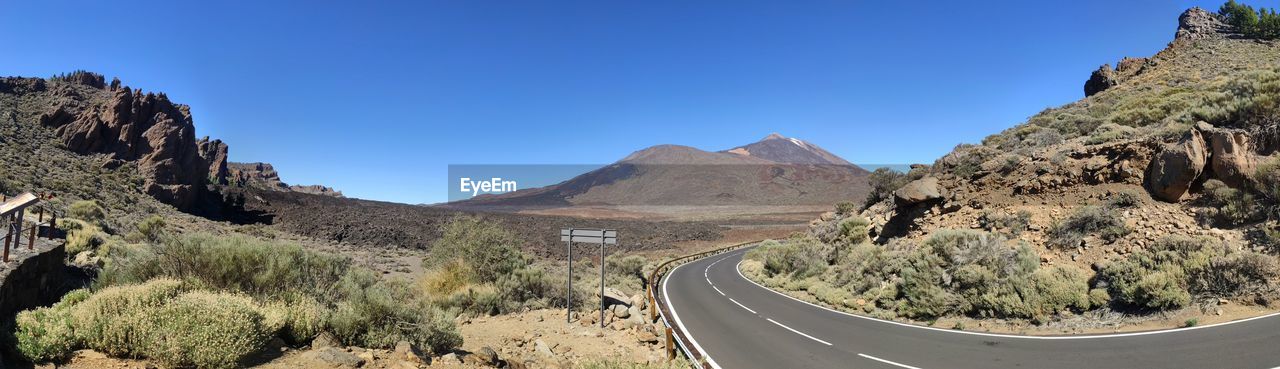 Panoramic view of road amidst mountains against clear blue sky