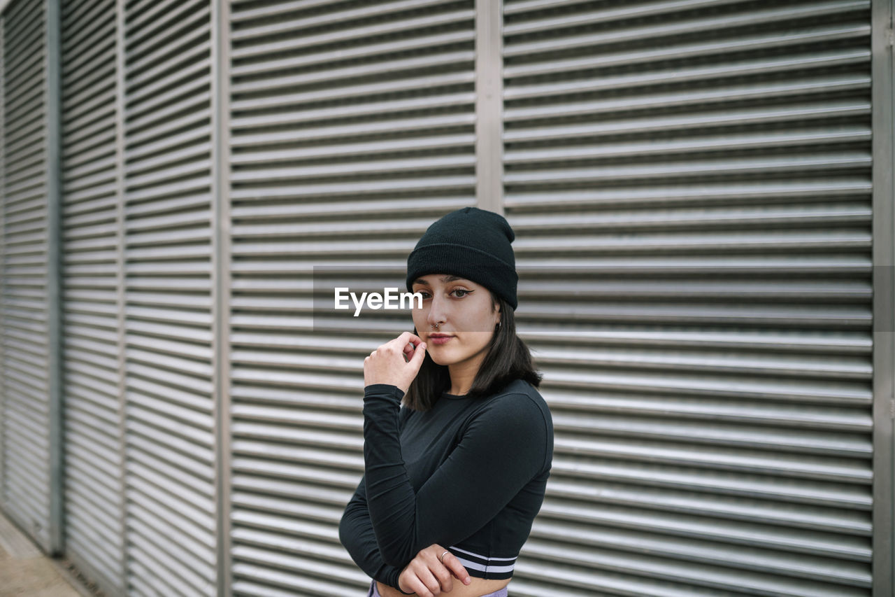Confident young woman in knit hat against metallic shutter