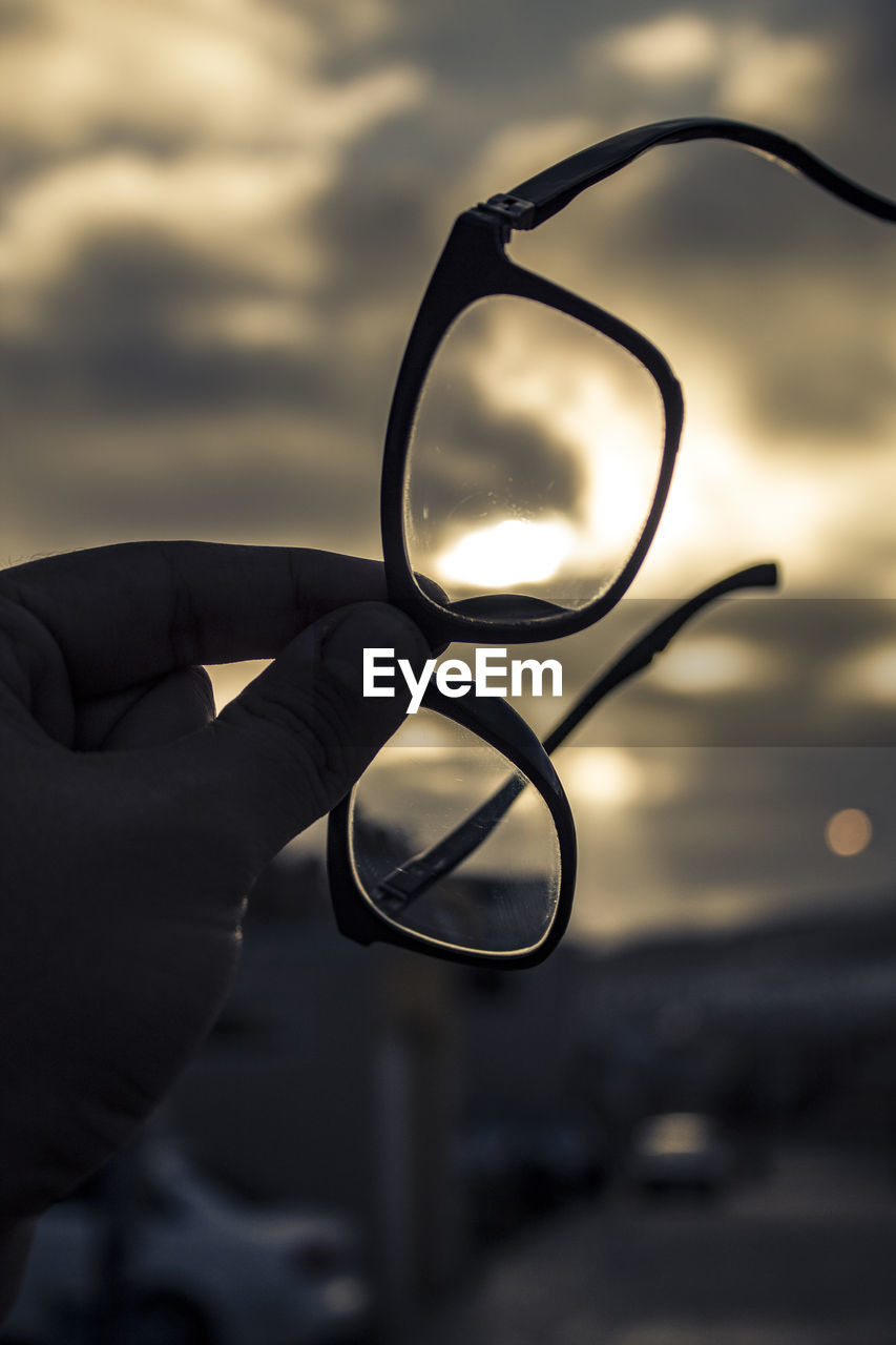 Cropped hand of person holding eyeglasses against sky