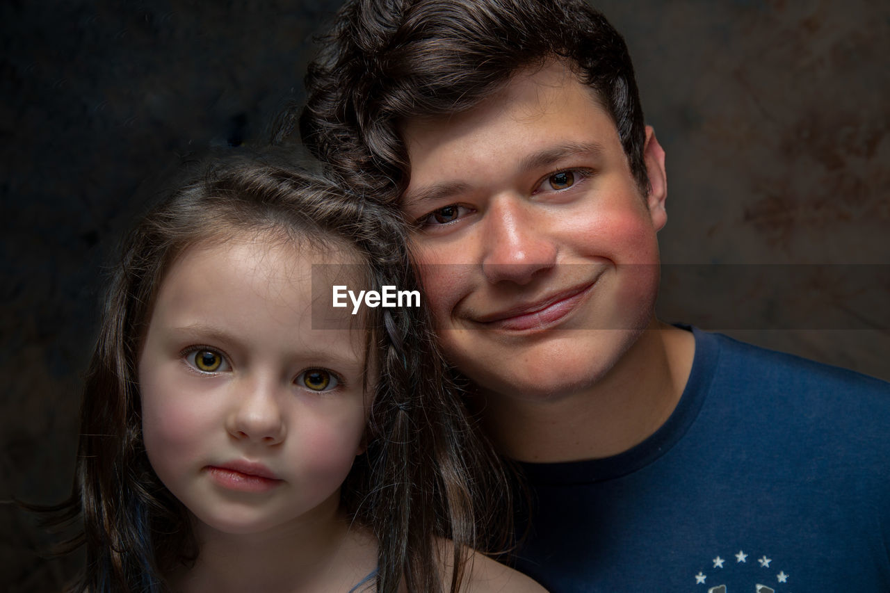 Portrait of smiling brother with cute sister against wall